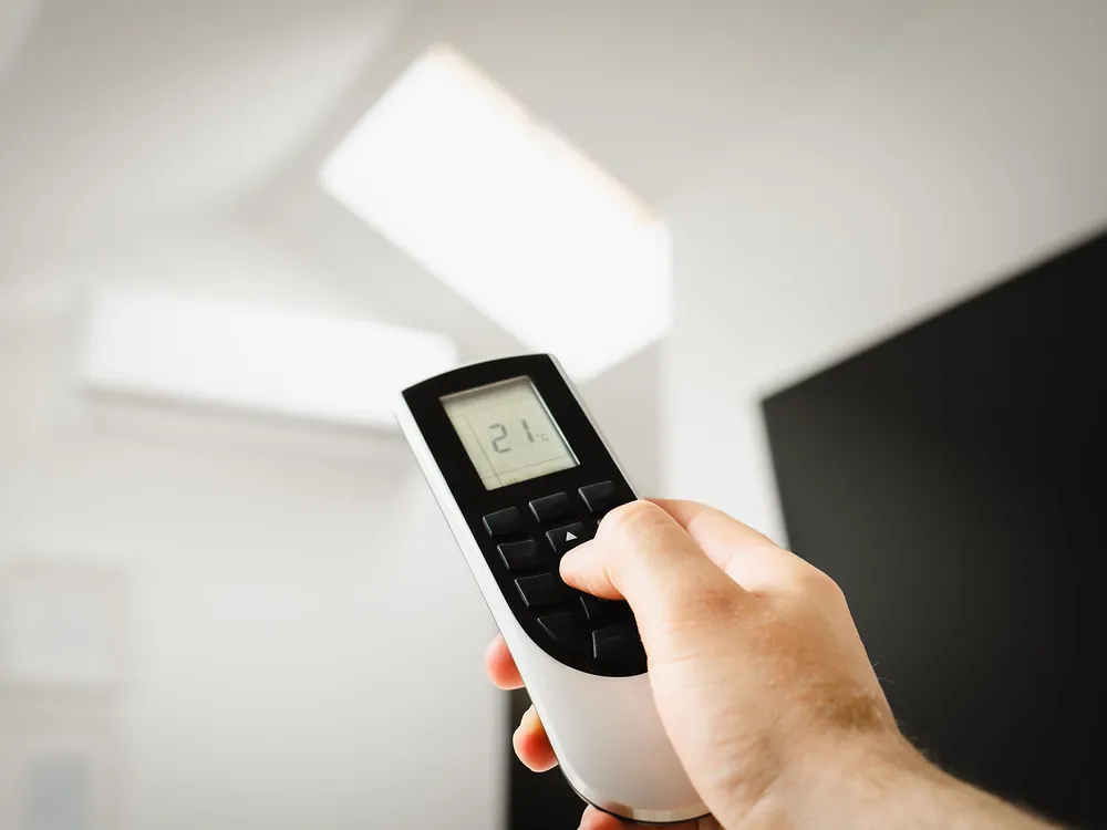 A hand pointing a remote at a wall-mounted AC