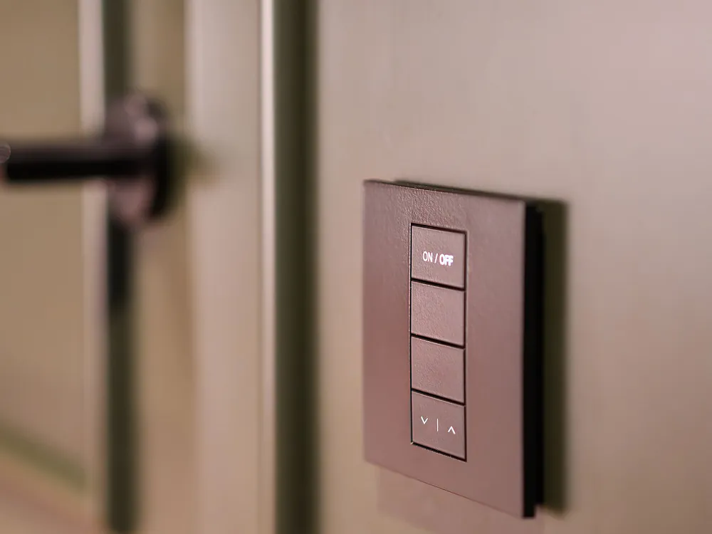 A dark glass smart switch panel on a wall beside a door handle