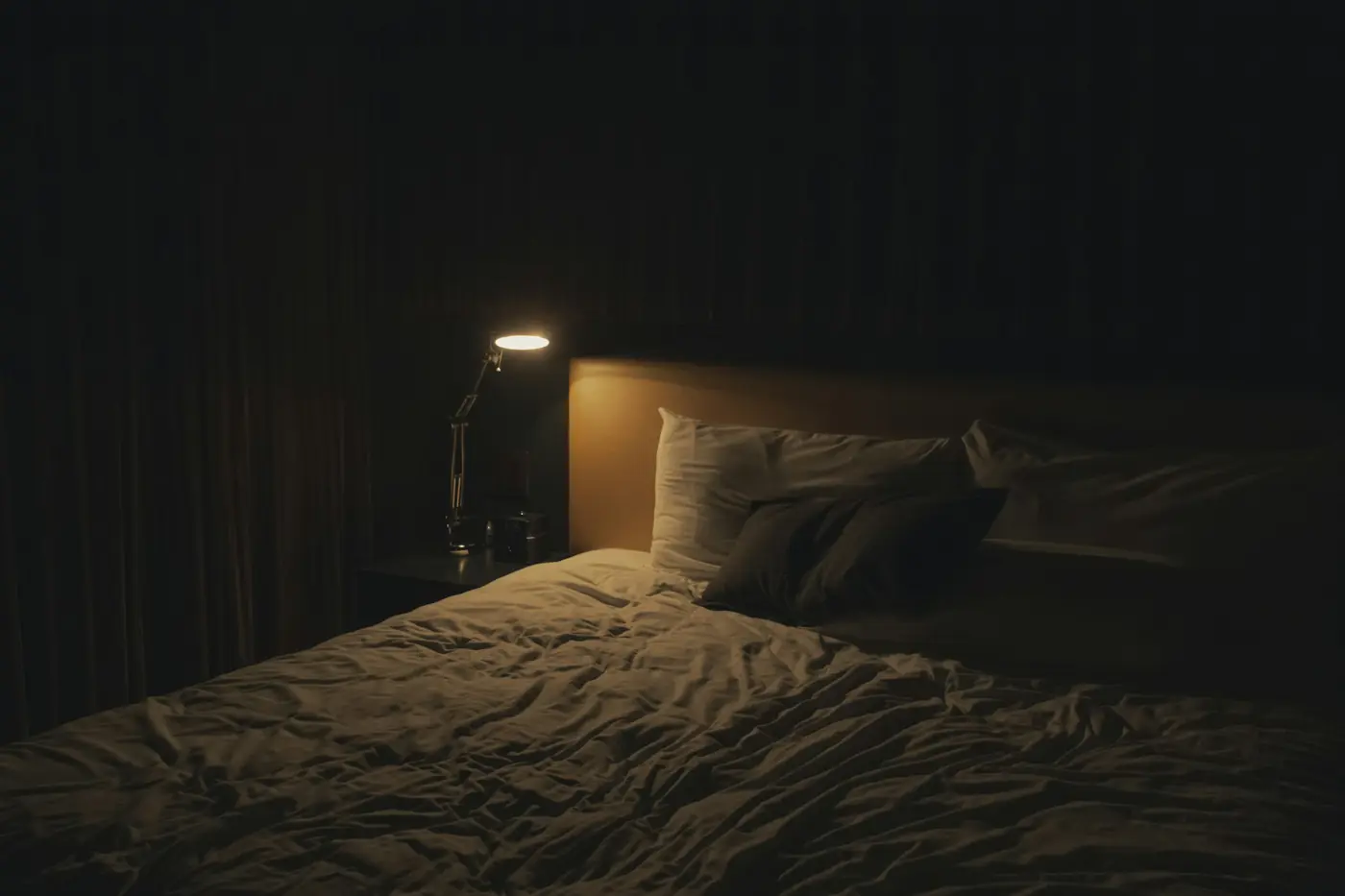A dark bedroom at night with a small lamp beside the bed